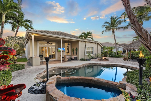 pool at dusk featuring a fire pit, a patio, ceiling fan, and an in ground hot tub