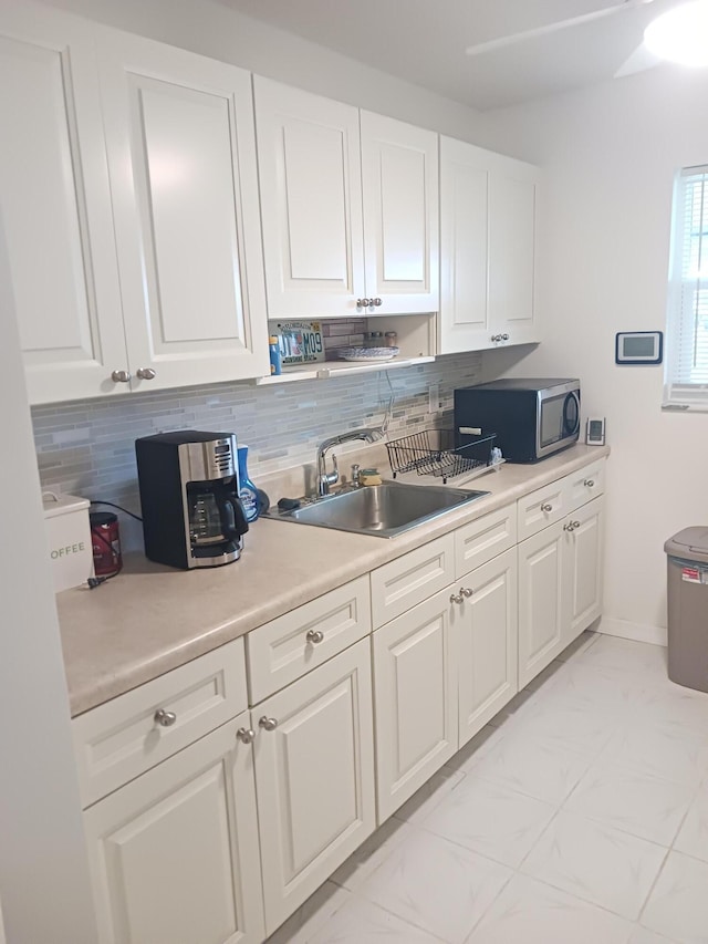 kitchen with white cabinets, stainless steel microwave, marble finish floor, light countertops, and a sink