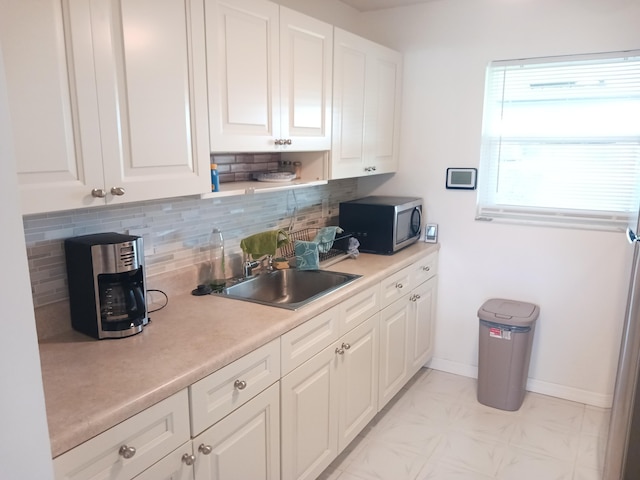 kitchen with light countertops, stainless steel microwave, a sink, and white cabinetry