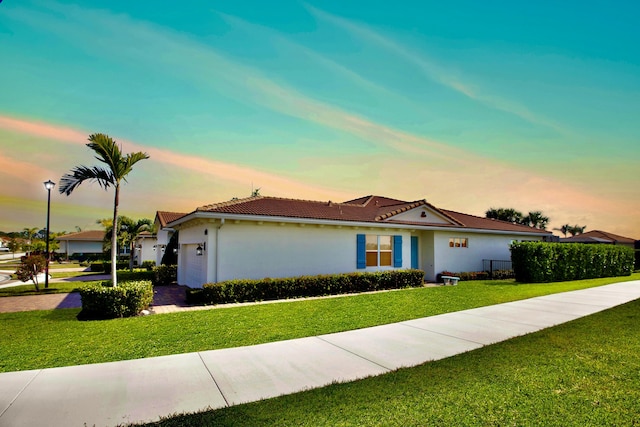 ranch-style home featuring a tile roof, driveway, stucco siding, a front lawn, and a garage