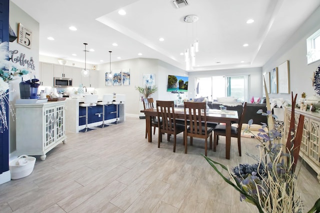 dining space featuring visible vents, light wood finished floors, baseboards, recessed lighting, and a tray ceiling