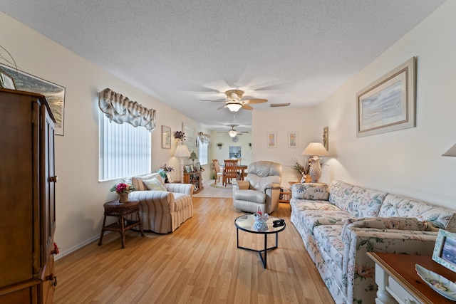 living room featuring ceiling fan, a textured ceiling, and light hardwood / wood-style floors