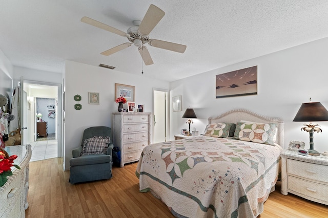 bedroom with ceiling fan, light hardwood / wood-style floors, and a textured ceiling