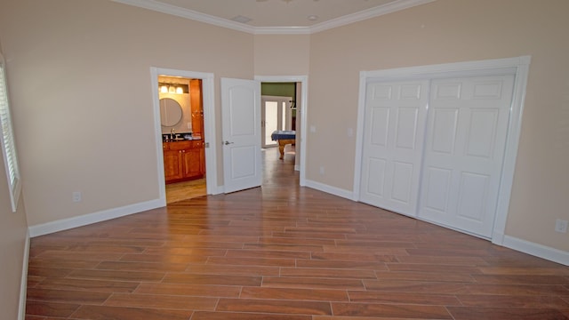 unfurnished bedroom with connected bathroom, dark wood-type flooring, crown molding, and a closet