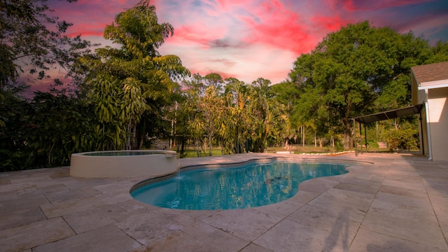 pool at dusk featuring an in ground hot tub and a patio area