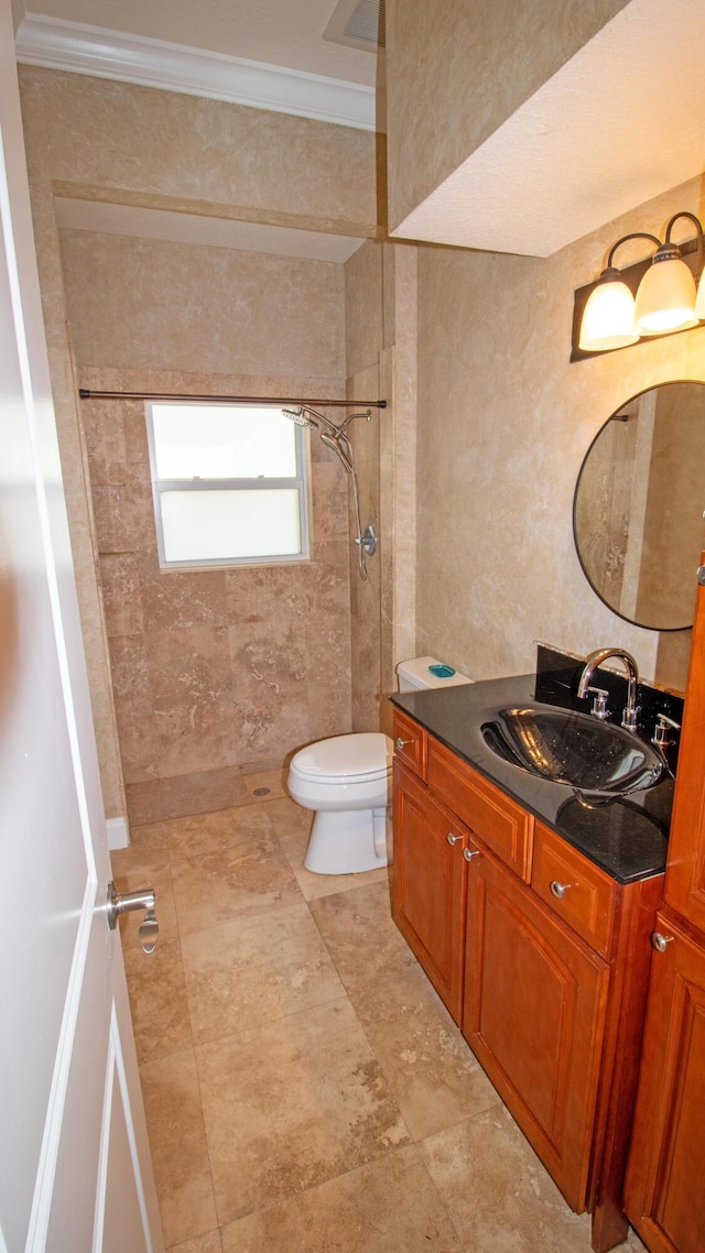 bathroom featuring toilet, tiled shower, vanity, and ornamental molding