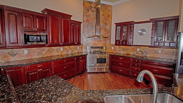 kitchen with wall chimney range hood, sink, dark stone counters, and range with two ovens