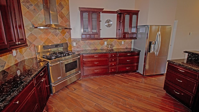 kitchen featuring tasteful backsplash, appliances with stainless steel finishes, dark stone counters, hardwood / wood-style floors, and wall chimney range hood