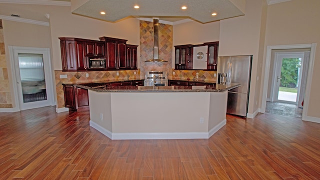 kitchen with crown molding, stainless steel appliances, wood-type flooring, and wall chimney range hood