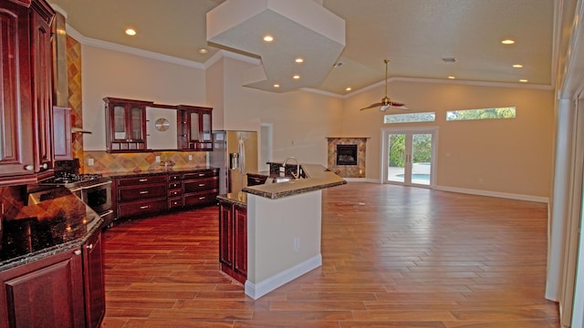 kitchen with crown molding, appliances with stainless steel finishes, dark stone countertops, a high end fireplace, and light wood-type flooring