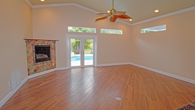 unfurnished living room featuring a tile fireplace, ornamental molding, ceiling fan, light hardwood / wood-style floors, and french doors