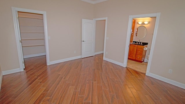 unfurnished bedroom featuring a closet, a walk in closet, sink, ensuite bathroom, and light hardwood / wood-style floors