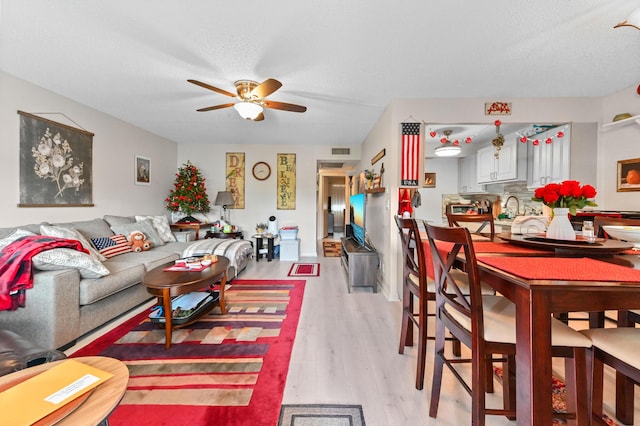 living room featuring ceiling fan, sink, light hardwood / wood-style floors, and a textured ceiling