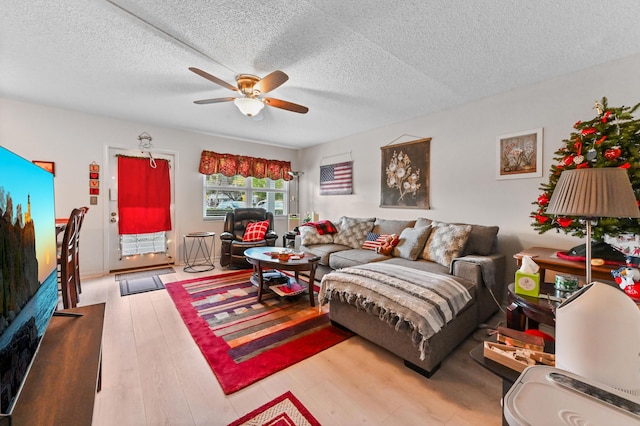 living room with ceiling fan, a textured ceiling, and light wood-type flooring