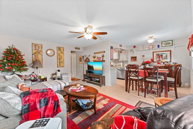 living room featuring ceiling fan, light hardwood / wood-style flooring, and a textured ceiling