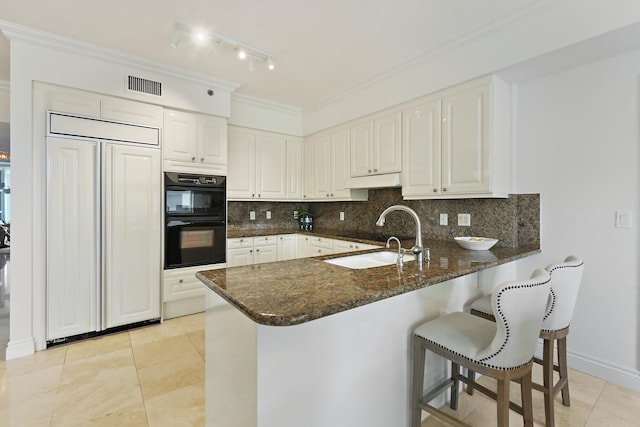 kitchen with black double oven, white cabinetry, sink, and kitchen peninsula