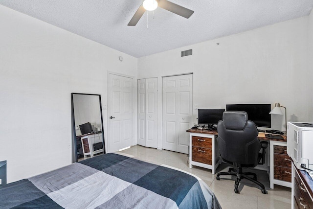 bedroom with ceiling fan, light tile patterned floors, a textured ceiling, and two closets