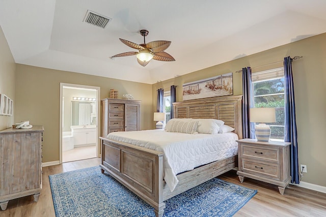 bedroom with multiple windows, a raised ceiling, light hardwood / wood-style floors, and ensuite bath