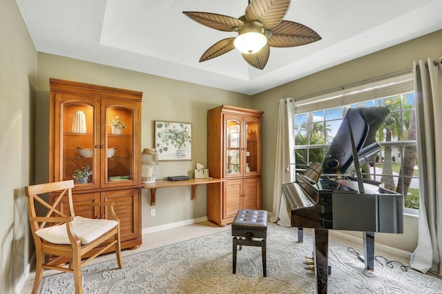 sitting room featuring a raised ceiling, ceiling fan, and light tile patterned flooring