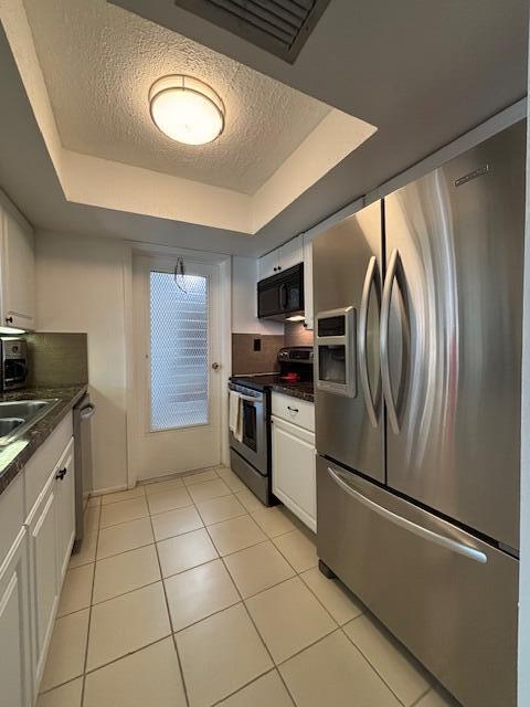 kitchen featuring a tray ceiling, stainless steel appliances, dark countertops, and light tile patterned floors