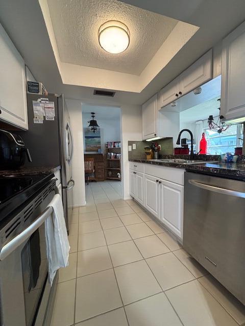 kitchen featuring a tray ceiling, light tile patterned flooring, a sink, decorative backsplash, and appliances with stainless steel finishes