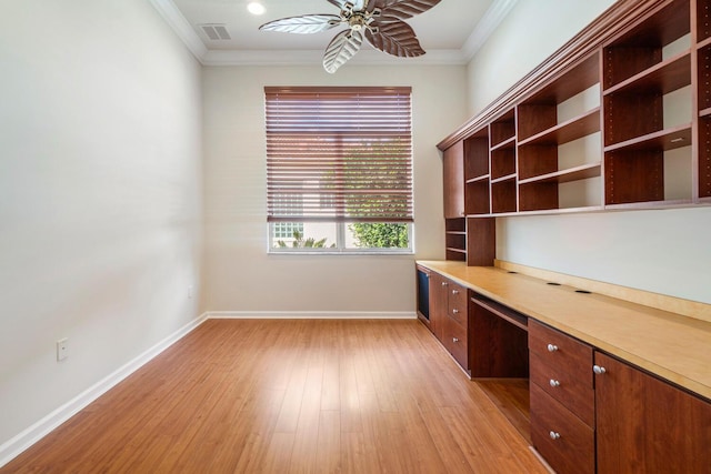 unfurnished office featuring light hardwood / wood-style flooring, built in desk, ornamental molding, and ceiling fan