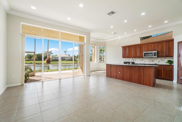 kitchen with sink, crown molding, a kitchen island with sink, a water view, and decorative backsplash