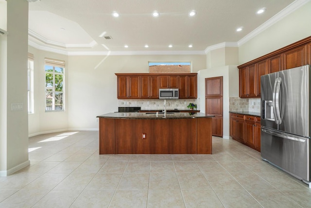 kitchen with light tile patterned floors, appliances with stainless steel finishes, ornamental molding, an island with sink, and dark stone counters