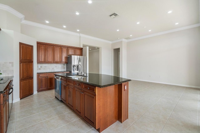 kitchen with sink, dark stone countertops, backsplash, stainless steel appliances, and a center island with sink