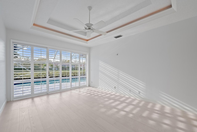 empty room with a tray ceiling, light hardwood / wood-style floors, and ceiling fan