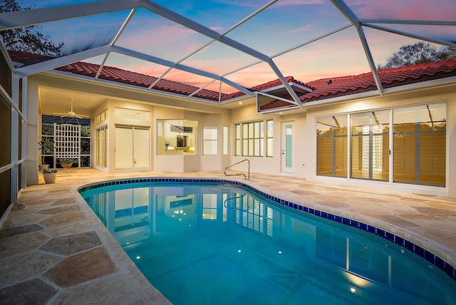 pool at dusk featuring a lanai, a patio, and ceiling fan