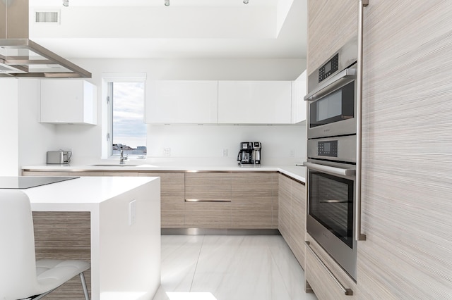 kitchen with black electric cooktop, sink, light brown cabinetry, and white cabinets