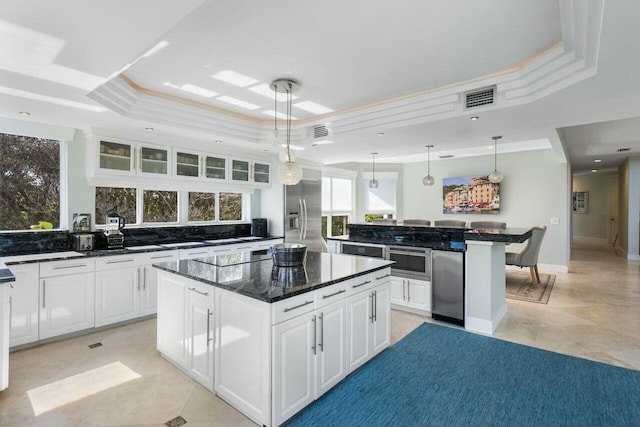 kitchen with white cabinetry, dark stone counters, hanging light fixtures, a center island, and a raised ceiling