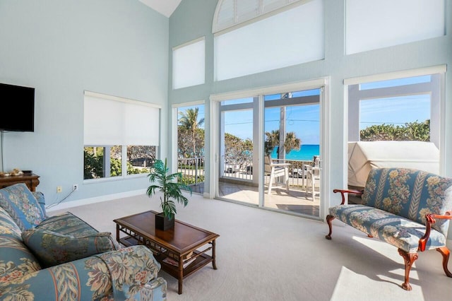 carpeted living room with a high ceiling, a healthy amount of sunlight, and a water view