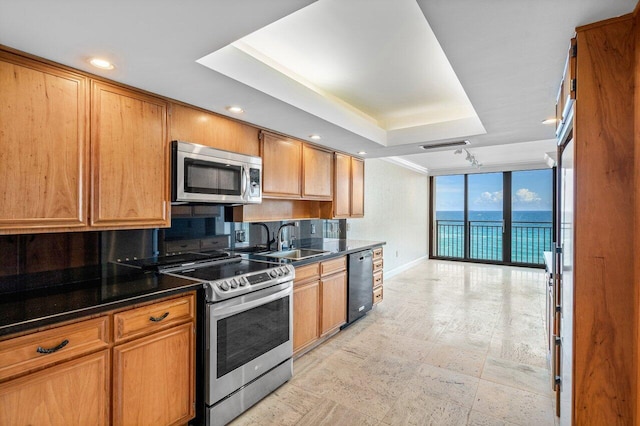 kitchen featuring a water view, a sink, appliances with stainless steel finishes, expansive windows, and dark countertops