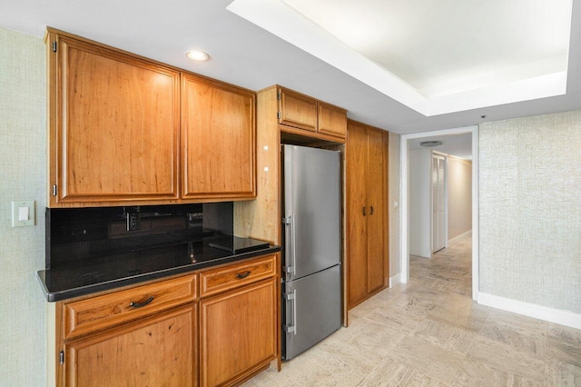 kitchen featuring brown cabinets, dark countertops, a raised ceiling, freestanding refrigerator, and baseboards