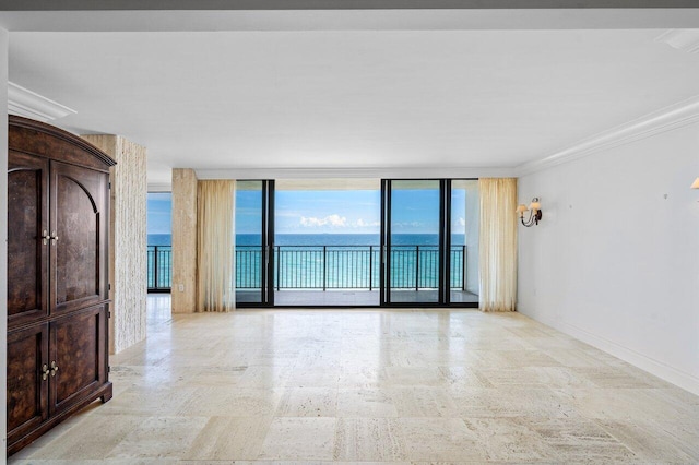 empty room with a water view, ornamental molding, stone finish flooring, a wall of windows, and baseboards