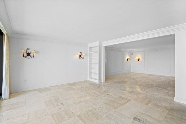 spare room featuring baseboards, ornamental molding, and a decorative wall