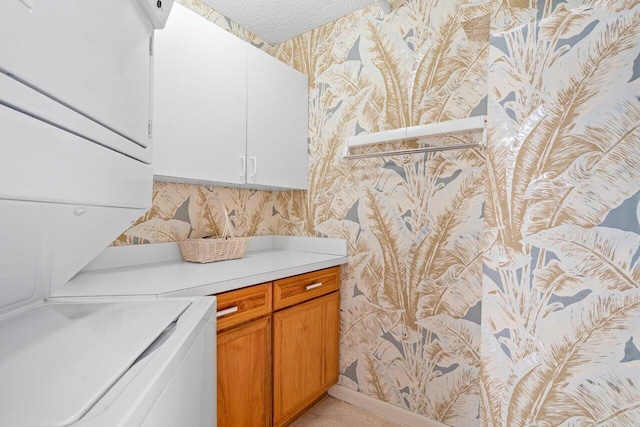 washroom featuring stacked washer / drying machine, cabinet space, a textured ceiling, and wallpapered walls