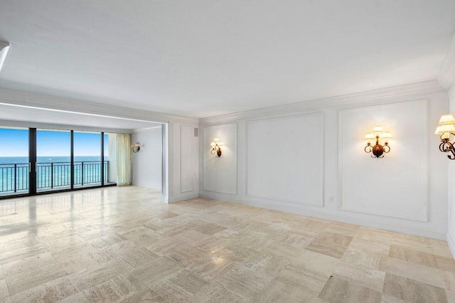 spare room with crown molding, a water view, a decorative wall, and a wall of windows