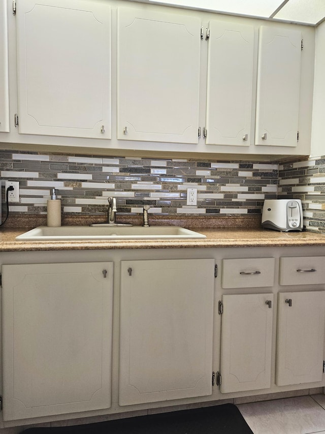 kitchen featuring tasteful backsplash, white cabinetry, and sink