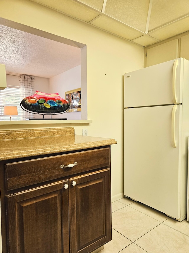 kitchen featuring a paneled ceiling, white refrigerator, light tile patterned floors, dark brown cabinets, and a textured ceiling