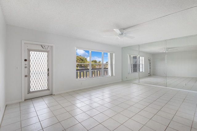 interior space with a textured ceiling, ceiling fan, and light tile patterned flooring