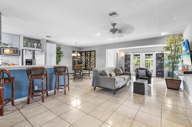 tiled living room with ceiling fan with notable chandelier, french doors, and a textured ceiling