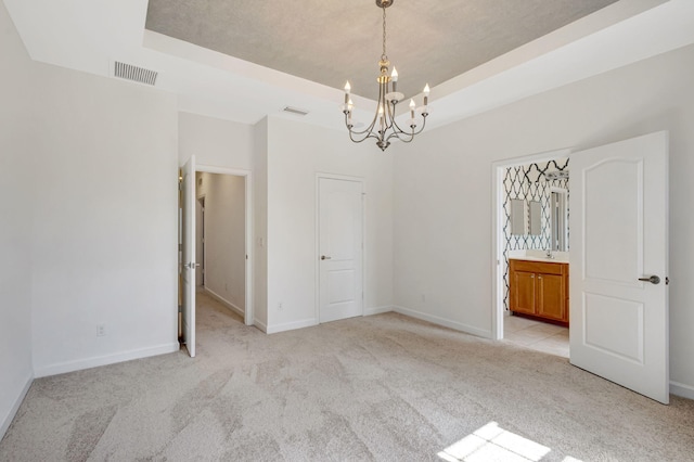 spare room featuring light carpet, a chandelier, and a tray ceiling