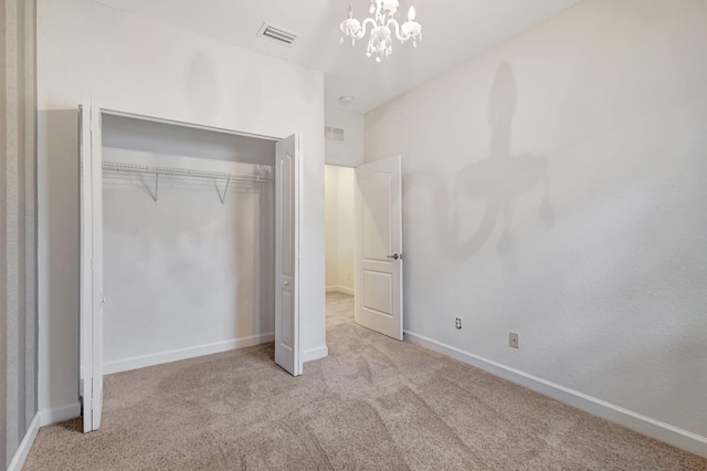 unfurnished bedroom featuring a closet, light carpet, and a notable chandelier