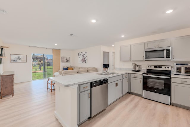 kitchen featuring appliances with stainless steel finishes, kitchen peninsula, sink, and light wood-type flooring