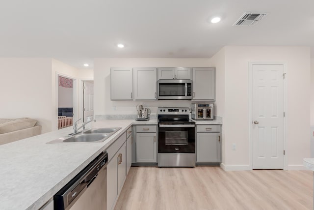 kitchen with sink, gray cabinets, stainless steel appliances, and light wood-type flooring