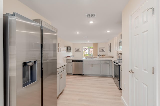 kitchen with stainless steel appliances, sink, light hardwood / wood-style flooring, and kitchen peninsula