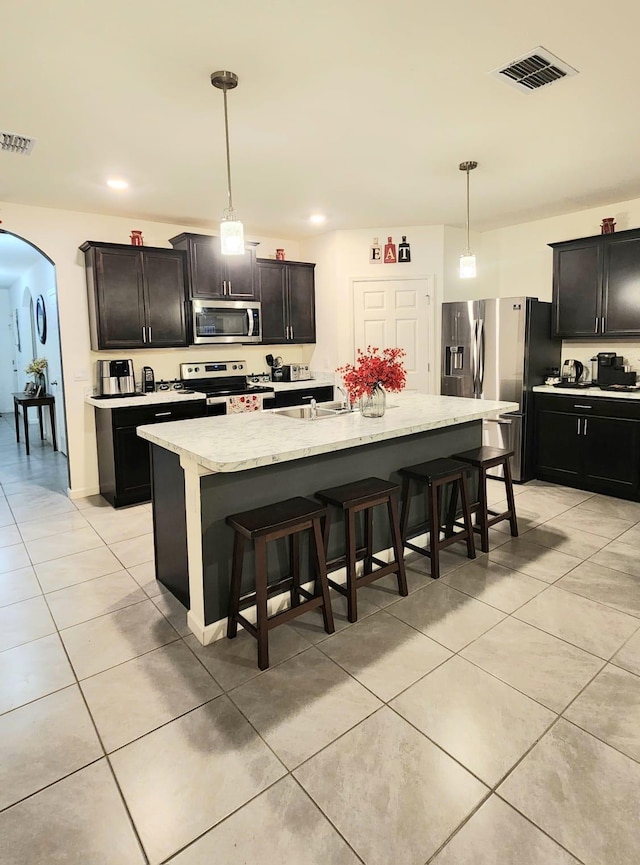 kitchen with pendant lighting, a kitchen island with sink, stainless steel appliances, and a kitchen bar